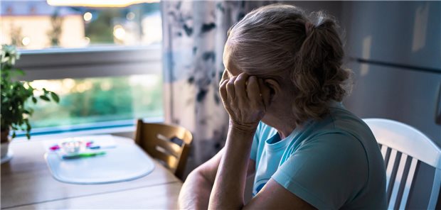 Ältere Frau sitzt am Küchtisch und schaut traurig aus dem Fenster heraus.