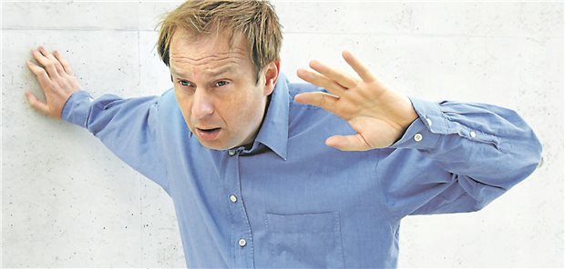 Ein Mann, dem schwindelig ist, stützt sich mit einer Hand an der Wand ab.