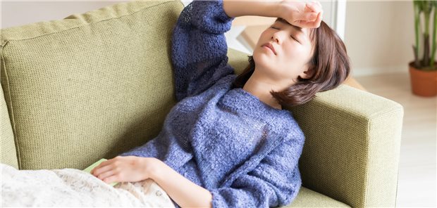 Eine junge Frau liegt auf dem Sofa und ist erschöpft.