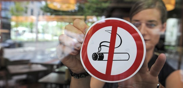 Rauchen wird uncooler Eine Frau befestigt einen "Rauchen-Verboten"-Aufkleber an einer Scheibe.
