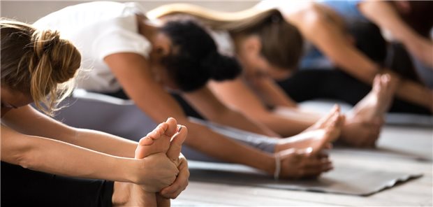 Eine Gruppe junger Frauen führen Dehnübungen im Fitnesstudio durch.