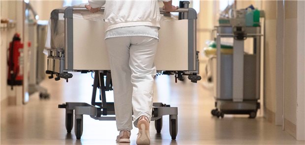 Eine Krankenpflegerin schiebt ein Krankenbett durch einen Flur.
