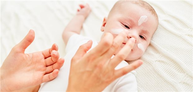 Eine Mutter cremt das Gesicht von ihrem Baby mit Hautcreme ein.