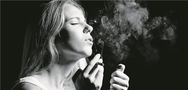 Eine Frau raucht einen Joint vor einem schwarzten Hintergrund.