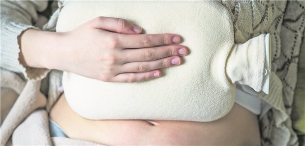 Man sieht den Bauch eine Frau, auf dem eine Wärmflasche liegt.