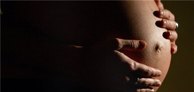 Eine hochschwangere Frau fasst sich mit beiden Händen an ihren Bauch.
