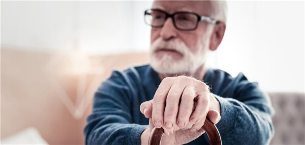Ein älterer Mann sitzt auf einem Sofa und stützt sich auf einen Gehstock.