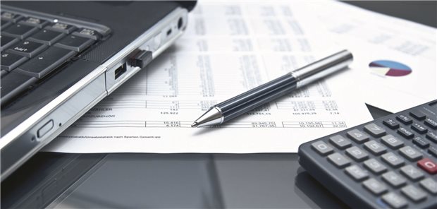 Ein Laptop, ein Stift und ein Taschenrechner liegen auf einem Tisch.