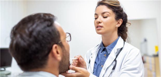 Ein Patient öffnet den Mund, damit die Ärztin seinen Rachen untersuchen kann. 