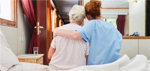 Krankenpflegerin umarmt Seniorin auf dem Bett sitzend im Hospiz