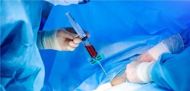 Ein Arzt hält eine große Spritze, die mit roter Flüssigkeit gefüllt ist. 