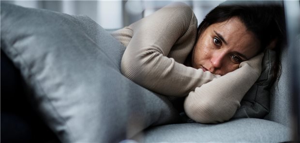 Eine Frau liegt auf einer Couch und starrt ins Leere.