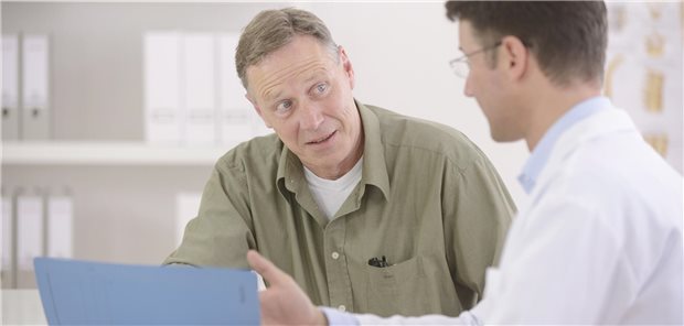 Ein Arzt hält einen Fragebogen in der Hand und unterhält sich mit einer patientin.
