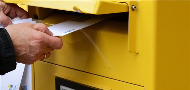 Ein Umschlag wird in einen Briefkasten geworfen.