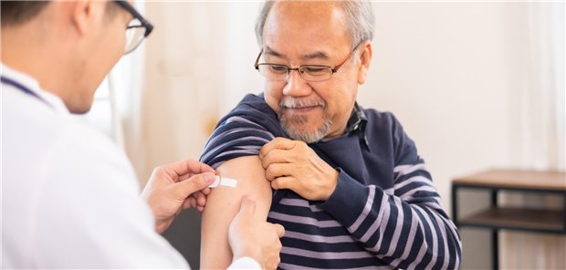 Ein Arzt klebt einem älteren Herrn ein Pflaster auf den Arm, wo der Mann geimpft wurde. 