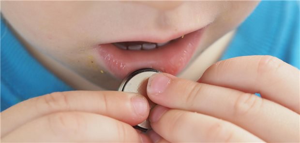 Ein Kind hält eine Knopfzelle an den Mund.