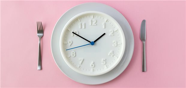 Eine Uhr auf einem Teller zeigt eine Uhrzeit an, wobei Messer und Gabel daneben liegen.