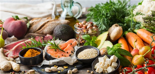 Viele gesunde Lebnesmittel, darunter Gemüse, Lachs und Sesam, liegen auf einem Tisch.