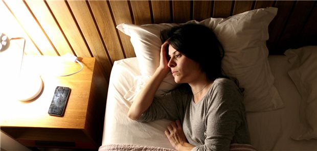 Eine Frau, die unter Schlaflosigkeit leidet, liegt wach in ihrem Bett und bertrachtet das angeschaltete Licht.