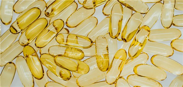 Draufsicht auf gelbe transparente Pillen mit Fischöl auf weißem Hintergrund. 