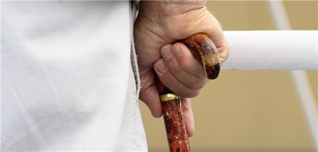 Die rechte Hand einer älteren Person hält sich am Griff eines Gehstockes fest.