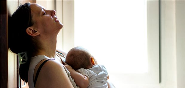 Eine Mutter hält ihr Kind im Arm. Sie sieht erschöpft aus und fasst sich an den Kopf.
