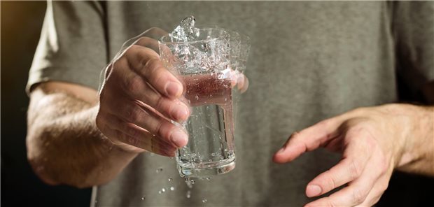Ein Mann hält mit zitternder Hand ein Glas Wasser. Das Konzept der Krankheit Morbus Parkinson und des damit verbundenen Tremors.