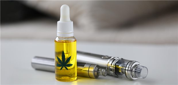 In einem kleinen Fläschchen ist eine helle Flüssigkeit zu sehen. Dahinter liegt eine E-Zigarette.