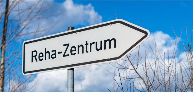 Weißes Straßenschild mit der Aufschrift Reha-Zentrum, dass den Weg weißt.