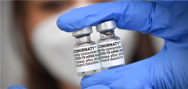 Eine Frau mit Mundschutz hält zwei Flaschen des Impfstoffs Cominraty in ihren Händen.