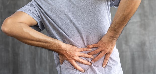 Ein junger Männer mit chronischen Schmerzen im unteren Rückenbereich greift sich an den Rücken.