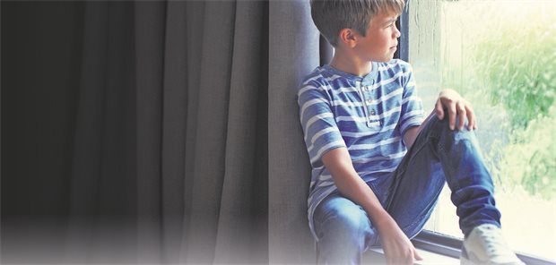 Ein kleiner Junge sitzt vor einem Fenster und schaut raus in den Garten.