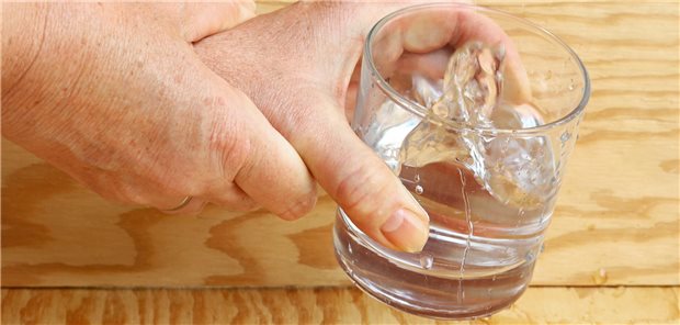 Eine Hand hält die andere, die vor zittern ein Wasserglas kaum halten kann.