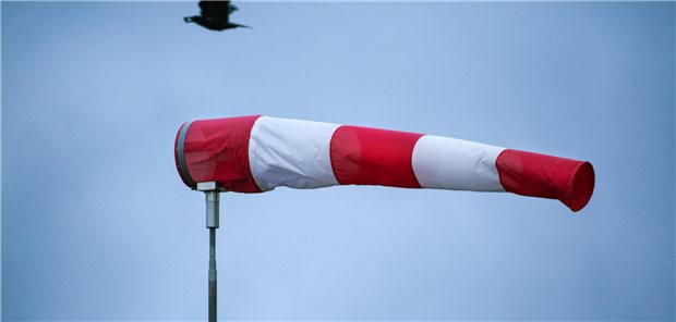 Windsack im Sturm, im Hintergrund fliegt eine Krähe