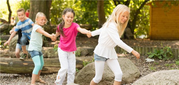 Kinder im Grundschulalter, die sich an den Händen halten und auf einem Spielplatz über Baumstämme klettern