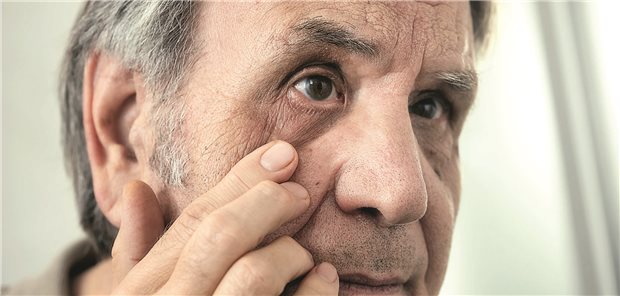 Ein älterer Herr schaut sich sein Auge im Spiegel an.