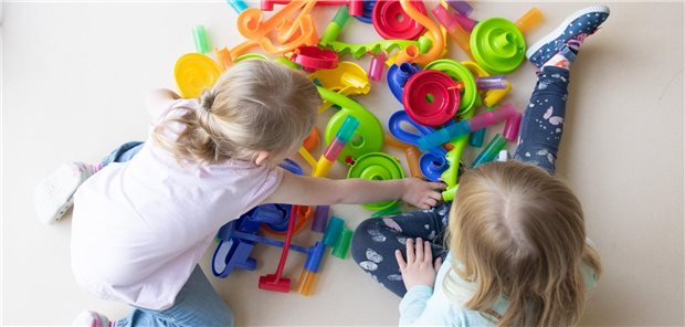 Zwei Kinder spielen am Boden mit diversen Spielzeugen.