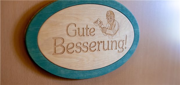 Sachsens Ärzte wollen MFA-Bonus und Weiterbildungsförderung Ein Türschild mit der Aufschrift "Gute Besserung" hängt an einem Behandlungszimmer in einer Hausarztpraxis.