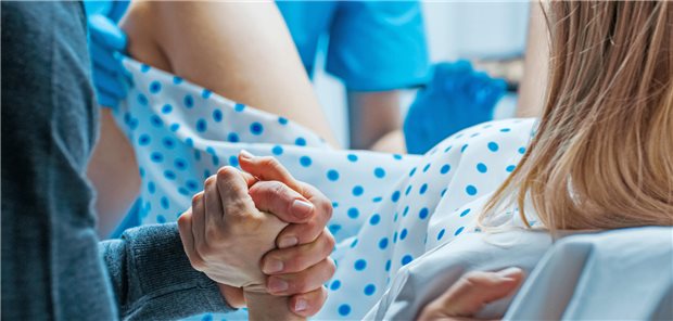 Eine Frau während einer Geburt, hält die Hand ihres Mannes fest.