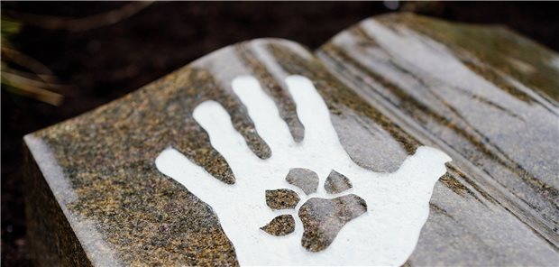Herr und Hund auch nach dem Tod auf dem Friedhof vereint Hand und Tierpfote – hier auf einem Mustergrab.