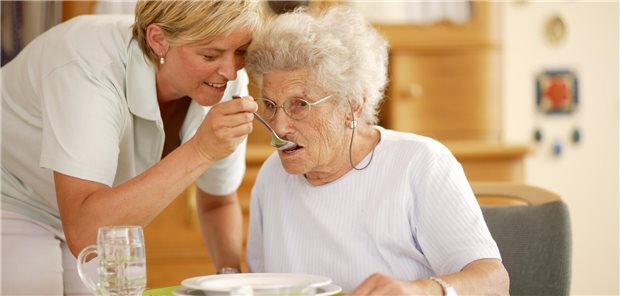 Pflegekraft hilft Seniorin beim Essen.
