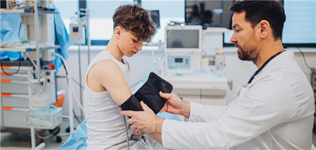 Ein Arzt legt einem Jungen eine Manschette um den rechten Arm.