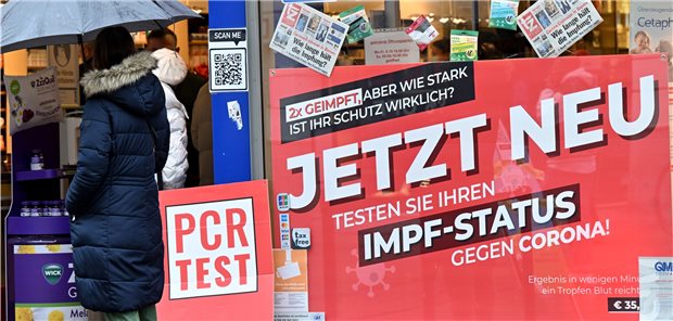Nur wenige Apotheken in Niedersachsen schaffen PoC-PCR-Testgeräte an Eine Frau wartet vor einer Apotheke, die PCR-Tests und einen Impfstatus-Test anbietet.