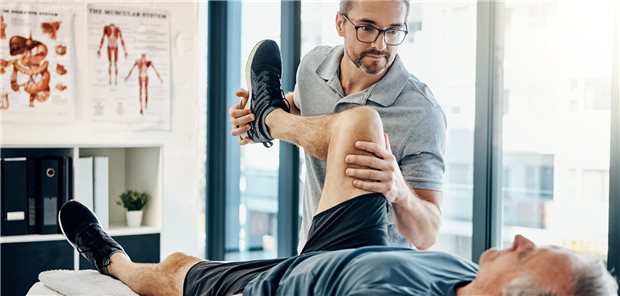 Das Foto zeigt einen Physiotherapeuten bei der Behandlung eines älteren Patienten.
