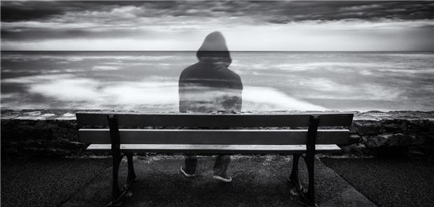 Ein nahezu durchsichtiger Mann sitzt auf einer Parkbank und schaut aufs Meer hinaus. 