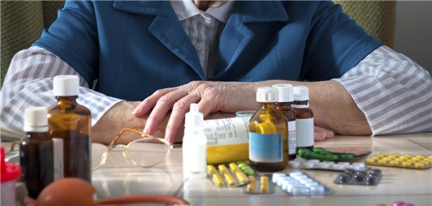 Eine ältere Person sitzt unschlüssig vor ihren Medikamenten.