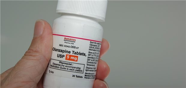 Eine Hand hält einen Behälter mit Olanzapin, einem atypischen antipsychotischen Medikament zur Behandlung von Schizophrenie und bipolarer Störung.