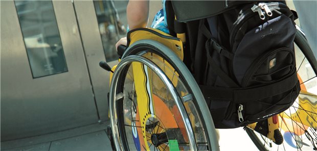 Mensch im Rollstuhl vor Gesundheitseinrichtung.