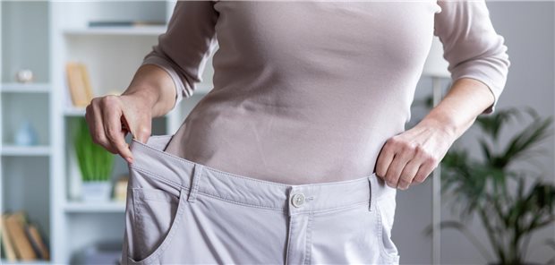 Frau zeigt ihre Gewichtsabnahme, indem sie eine übergroße Hose hochhält.