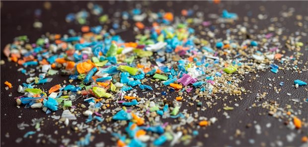Zahlreiche kleine bunte Partikel von Plastik liegen auf einer dunklen Oberfläche